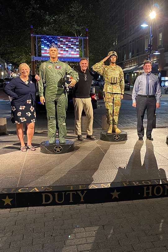 Larry Schneider standing with a USA troops memorial