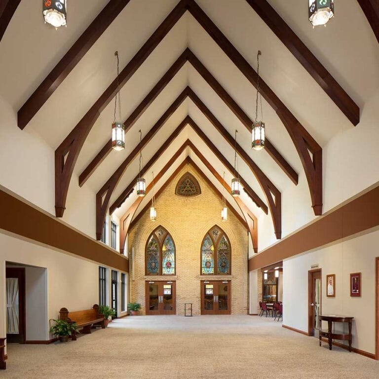 Catholic Architectural design cues are on display with stained glass, pointed arch windows, and heavy timber beams in the Fellowship Hall of St. Clare of Assisi Catholic Church in Monroe, Wisconsin